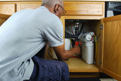 Mature man with wrench tighten pipes under sink at home