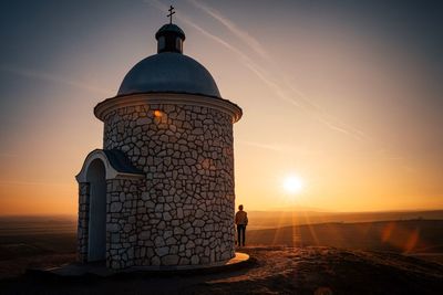 Man standing by church against sky during sunset