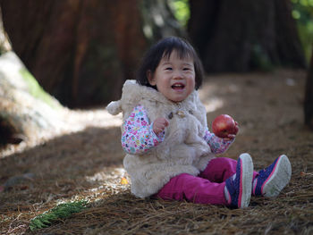 Portrait of cheerful baby girl holding apple while sitting on field