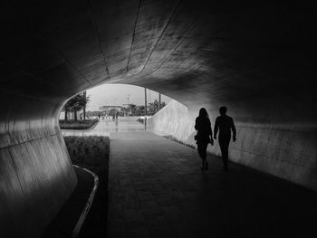 Rear view of silhouette people walking on footpath in tunnel