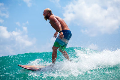 Shirtless man surfing on sea against sky