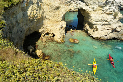 People canoeing in sea against rock formation