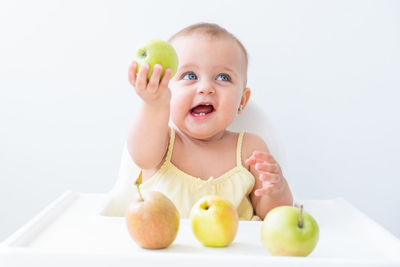 Portrait of cute boy eating granny smith apple on table against white background