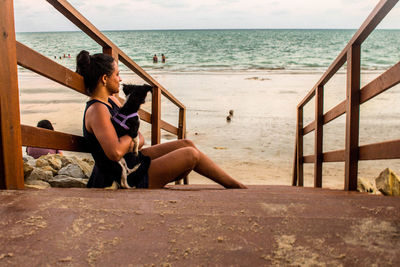 People sitting on shore at beach against sky