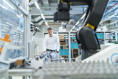 Businessman in a modern factory hall looking at robot