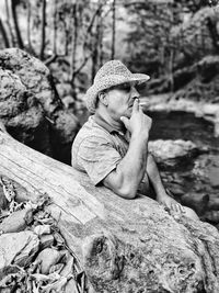 Man smoking cigarette while sitting by log in forest