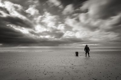 Rear view of man standing at beach against cloudy sky