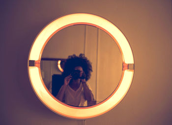 Portrait of woman photographing illuminated mirror