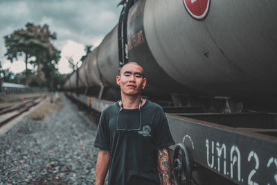 Portrait of young man standing by car against sky
