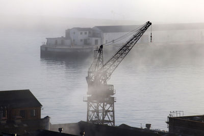 Cranes on pier by sea against sky