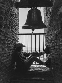 Side view full length of young woman sitting amidst walls by bell