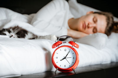  woman sleeping with pet cat close up of alarm clock, morning time, wake up, female healthy lifestyle