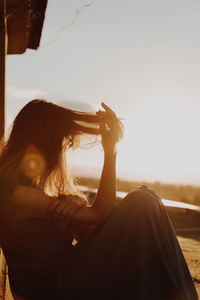 Side view of woman sitting on terrace against sky