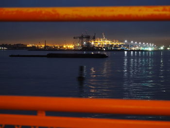 Illuminated harbor by sea against sky at night