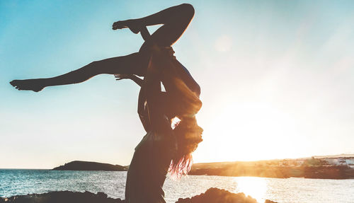 Woman with arms outstretched against sea at sunset