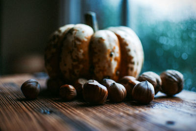 Close-up of chestnuts and pumpkin on wooden table by window