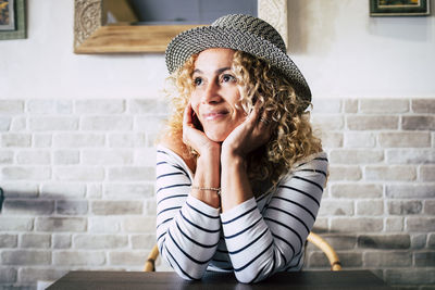 Portrait of smiling young woman sitting against brick wall