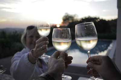 Close-up of hand holding beer glass against sky during sunset