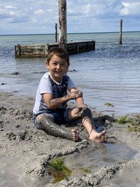 Portrait of boy sitting in mud on beach