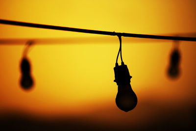 Close-up of light bulbs hanging against sky during sunset