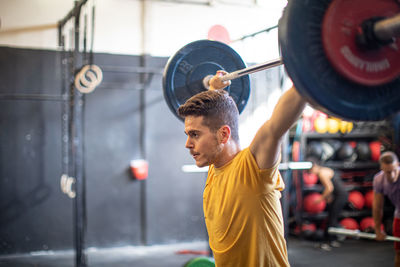 Muscular guy lifting barbell in modern gym