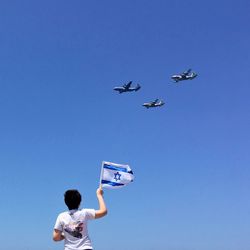 Low angle view of boy with israeli flag looking at airplane against sky