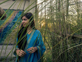 Smiling teenage girl looking away while standing by plants