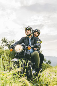 Couple looking away while sitting on motorcycle against sky
