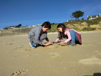 Friends playing on wet sand at beach against clear blue sky during sunny day