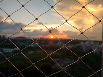 Close-up of chainlink fence against sunset sky