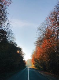 Country road amidst trees against sky during autumn