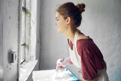 Side view of young woman standing against wall