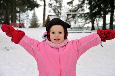 Portrait of girl with arms outstretched standing on snow covered field