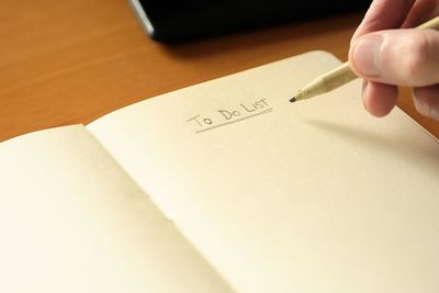 Cropped hand of man writing in notepad at desk in office