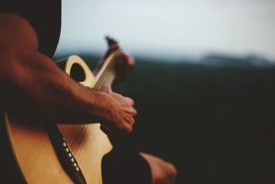 Midsection of man playing guitar against sky