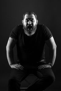 Portrait of man sitting against black background