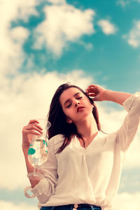 Beautiful young woman drinking glass against sky