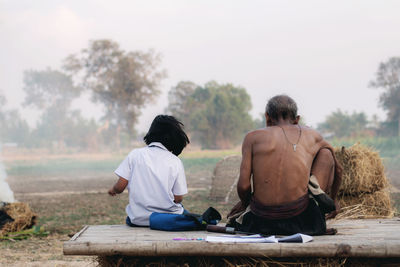 Rear view of people sitting on landscape against sky