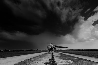 Man practicing handstand on wet road against storm cloud