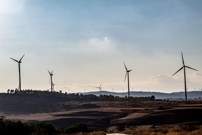 Wind turbines on field against sky during sunset