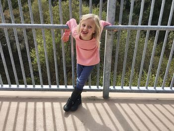 Playful girl leaning on railing of bridge over trees