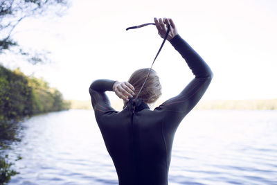 Rear view of female swimmer wearing wetsuit at lakeshore