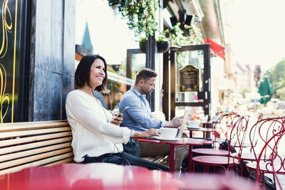 Thoughtful businesswoman holding smart phone while sitting at sidewalk cafe