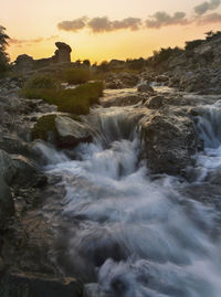 Scenic view of waterfall against sky during sunset