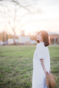 Side view of woman with eyes closed standing on field against sky during sunset