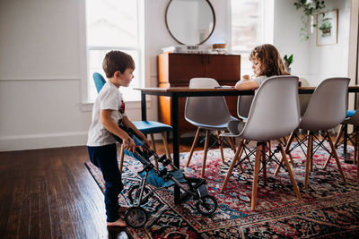 Young brother showing stuffed animal in stroller to sister at home