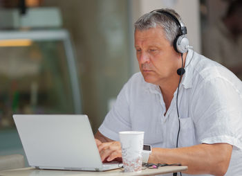 Mature man using laptop while sitting in sidewalk cafe