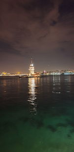 Illuminated city by sea against sky at night