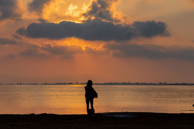 Silhouette woman standing on beach against sky during sunset