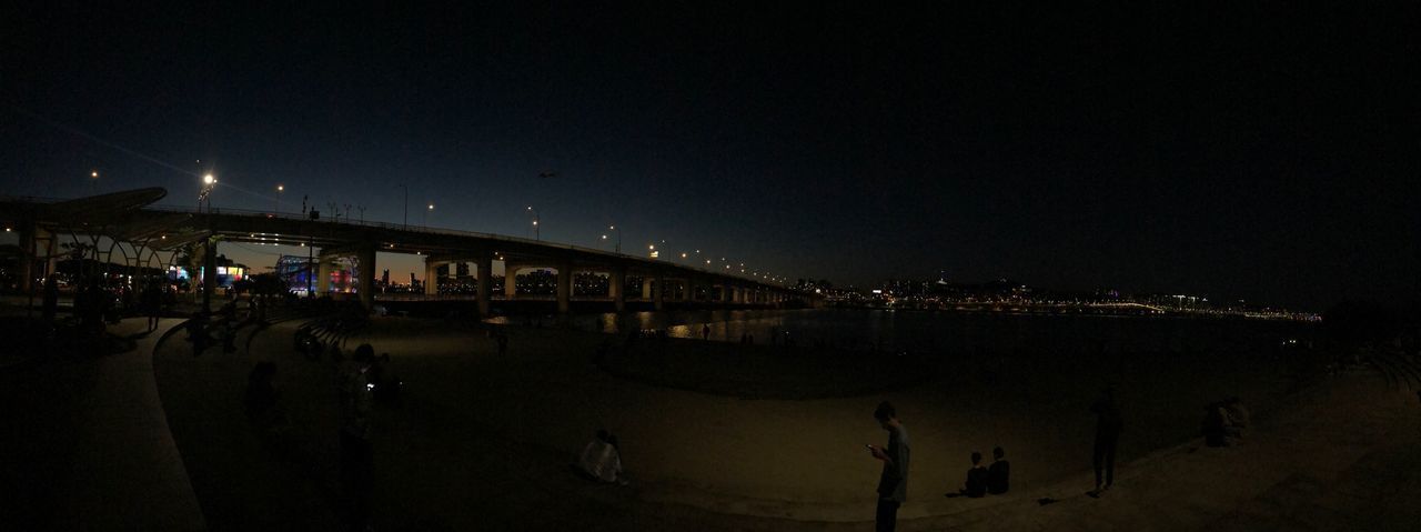 PEOPLE AT ILLUMINATED BRIDGE AGAINST SKY AT NIGHT